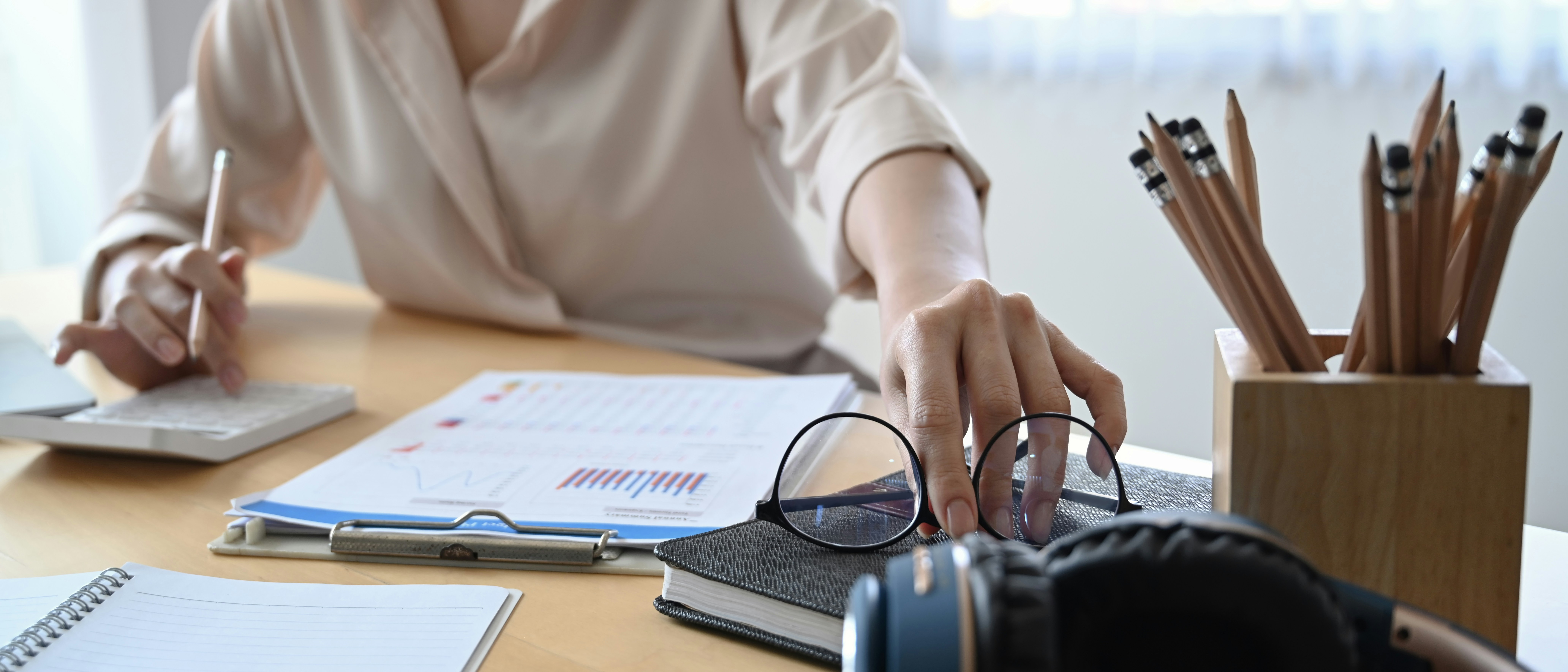 Woman sitting at desk on laptop, reaching for glasses